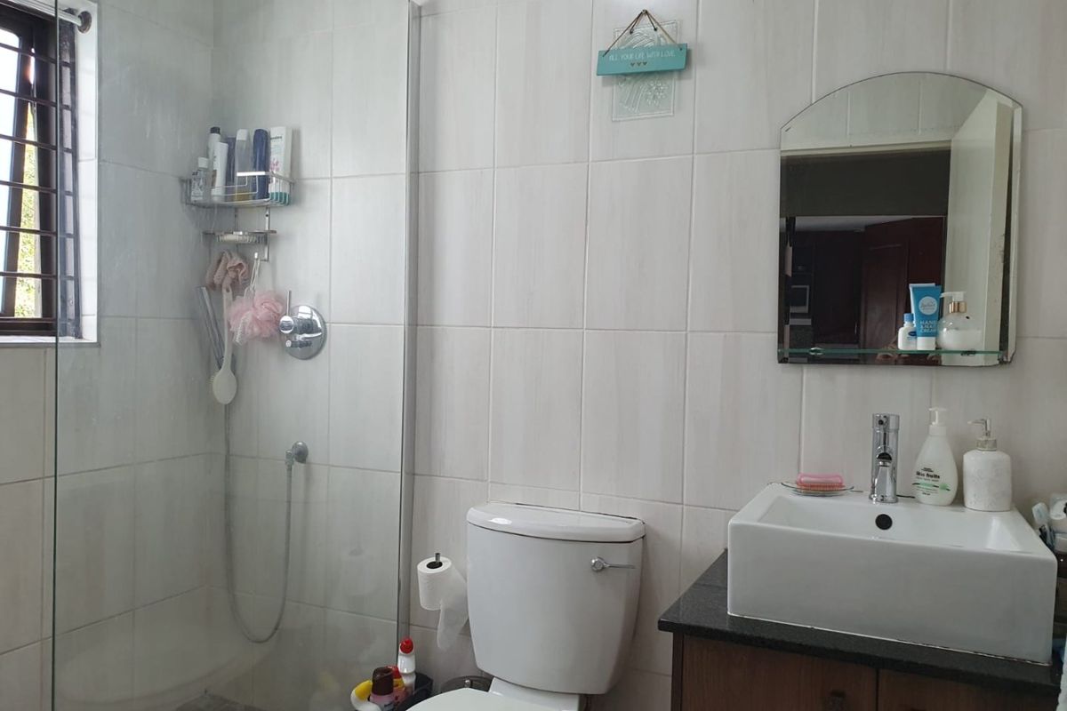 A functional bathroom featuring a glass-enclosed shower, a modern countertop basin with vanity storage, and neutral wall tiling.