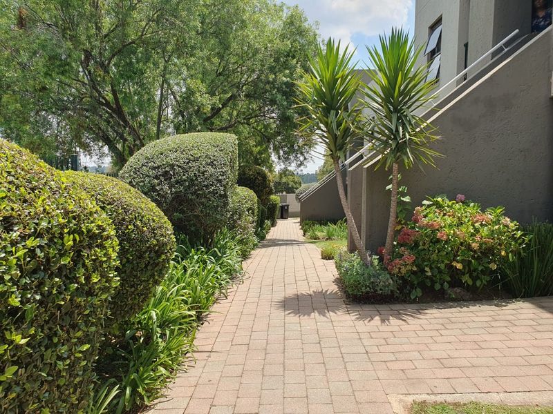 A well-maintained paved walkway leading through a landscaped garden area alongside the apartment building exterior.