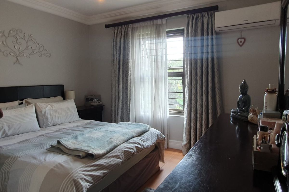 A well-maintained bedroom featuring laminate flooring, decorative coving, and a wall-mounted split-system air conditioner.