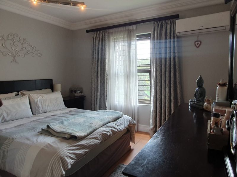 A well-maintained bedroom featuring laminate flooring, decorative coving, and a wall-mounted split-system air conditioner.