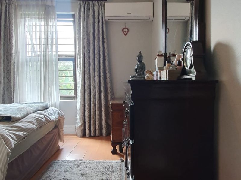 A well-maintained bedroom featuring timber flooring, decorative cornice detailing, and a wall-mounted split-system air conditioner for climate control.