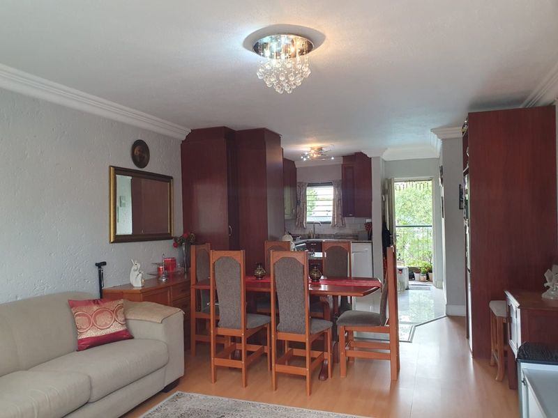 Open-plan living and dining area featuring laminate flooring, coving, and direct access to a balcony, with an integrated kitchen space.
