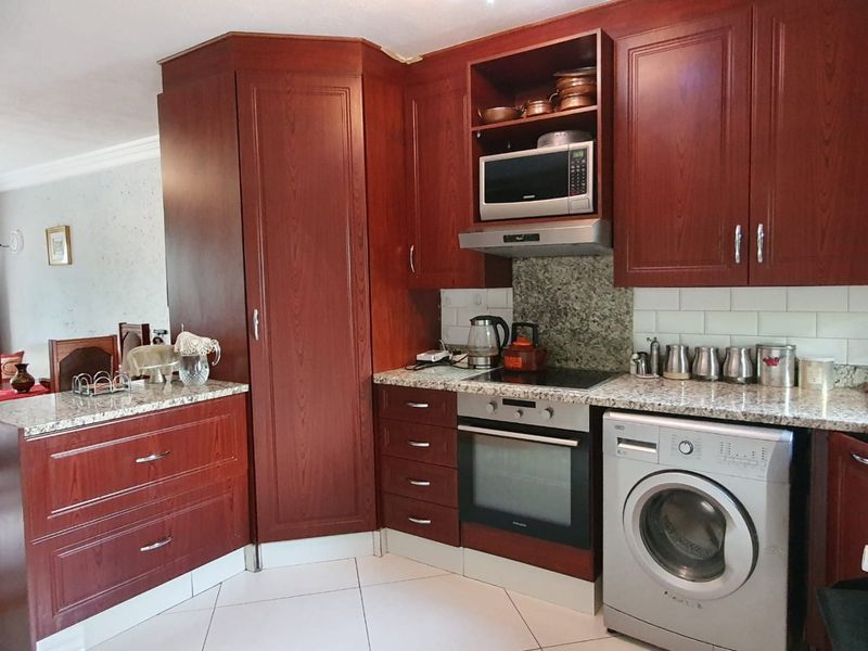 A functional kitchen featuring dark wood cabinetry, granite countertops, a subway tile backsplash, and integrated appliances including an oven, hob, and extractor fan.
