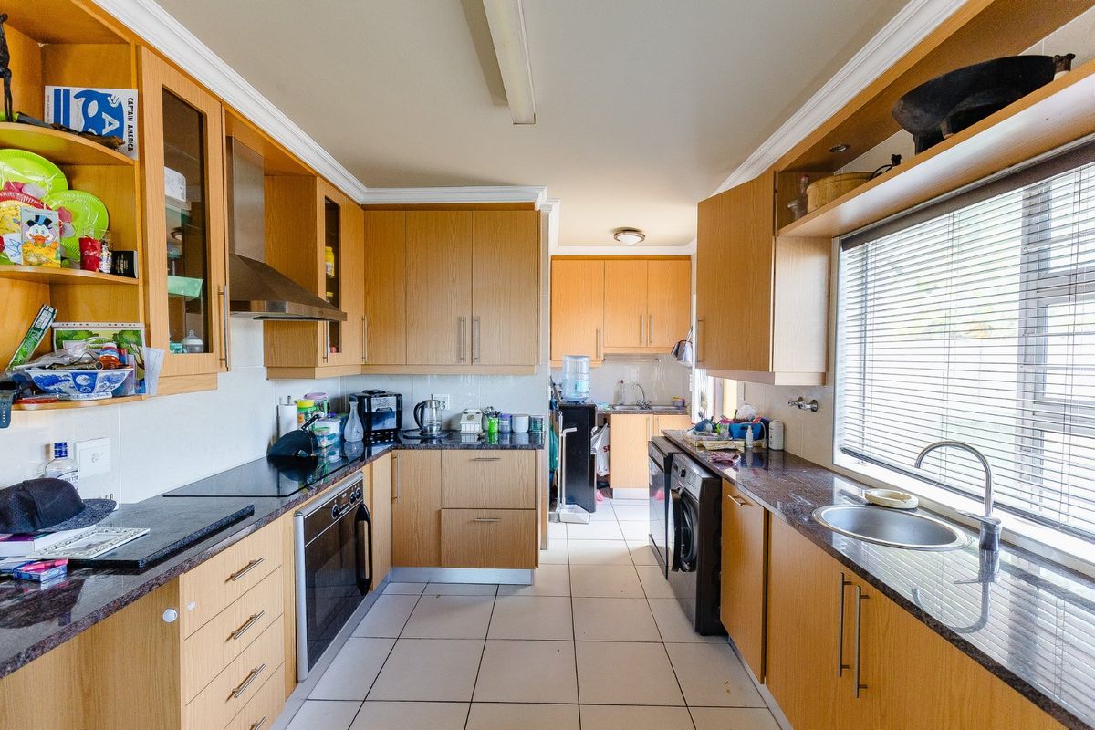 A functional galley-style kitchen featuring light wood cabinetry, dark granite countertops, built-in oven, hob, extractor fan, and a stainless steel sink.
