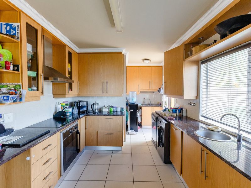 A functional galley-style kitchen featuring light wood cabinetry, dark granite countertops, built-in oven, hob, extractor fan, and a stainless steel sink.
