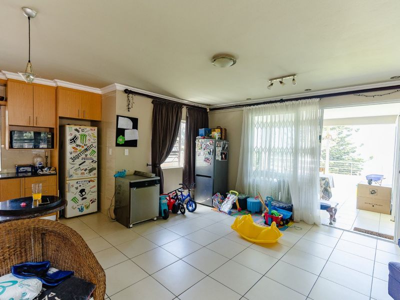 Open-plan living and kitchen area featuring tiled flooring, built-in wooden cabinetry, and direct access to an outdoor patio through sliding glass doors.