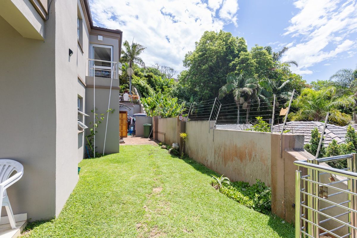 A side garden area featuring a lawn, perimeter boundary wall with electric fencing, and access to the rear of the townhouse.