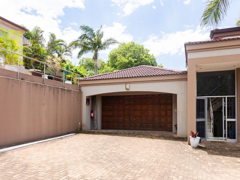 Exterior view of the townhouse featuring a paved driveway, a single garage with a wooden door, and a tall retaining wall.