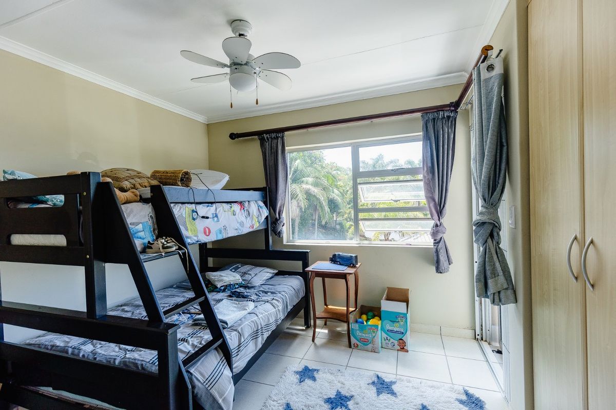 A bedroom featuring tiled flooring, a ceiling fan, and built-in cupboards, with natural light provided by a large window.