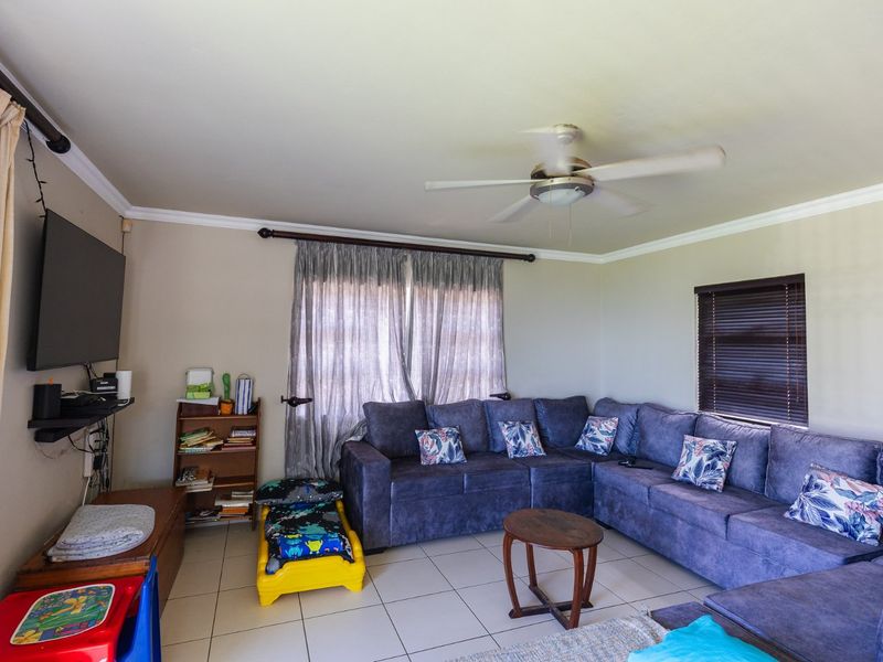 A comfortable living room featuring tiled flooring, crown molding, and a ceiling fan, providing a functional space for relaxation.