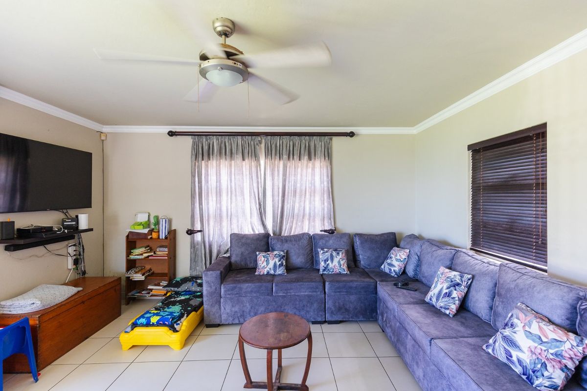 A comfortable living room featuring tiled flooring, a ceiling fan, and crown molding, providing a functional space for relaxation.
