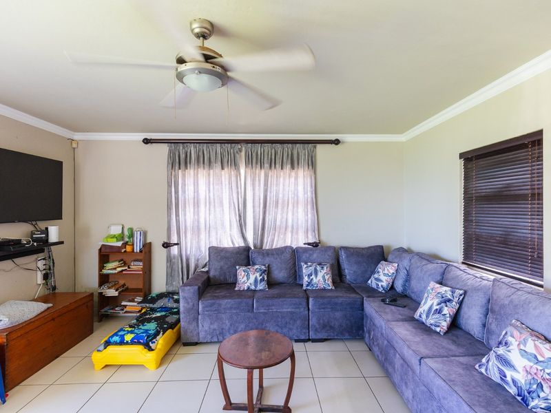 A comfortable living room featuring tiled flooring, a ceiling fan, and crown molding, providing a functional space for relaxation.