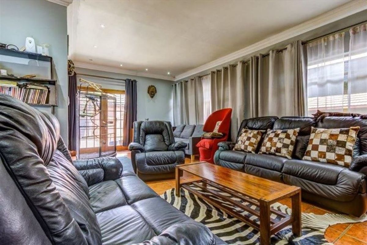 A comfortable living room featuring tiled flooring, recessed downlighting, crown molding, and access to the outdoors via glass-paneled french doors.