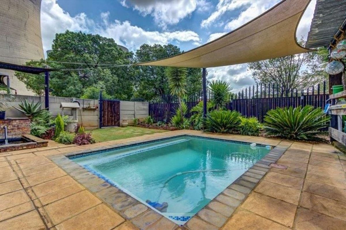 Outdoor pool area featuring a paved patio, shade sail, and established garden landscaping with perimeter fencing.