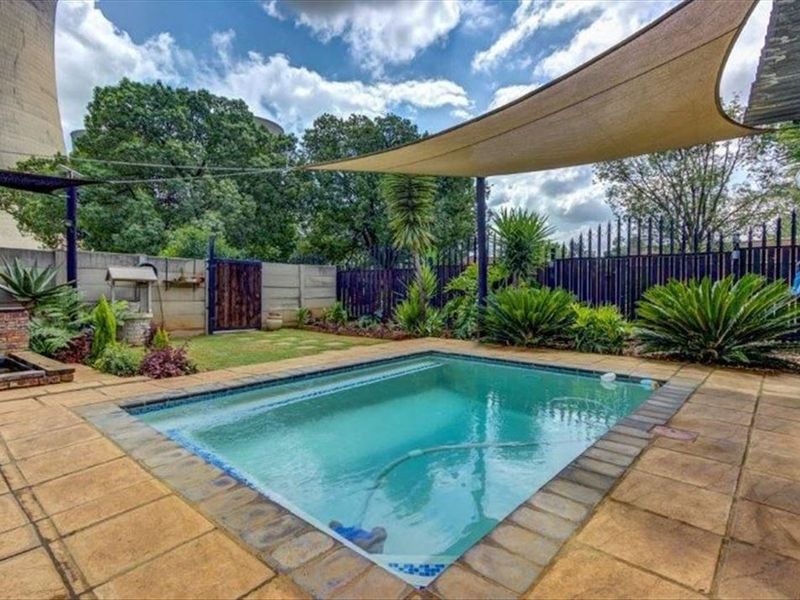 Outdoor pool area featuring a paved patio, shade sail, and established garden landscaping with perimeter fencing.