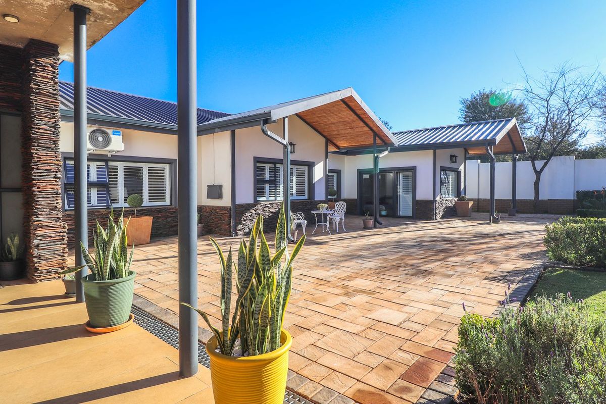 A spacious rear patio area featuring stone cladding, paved flooring, and covered sections with timber ceilings, overlooking a well-maintained garden.