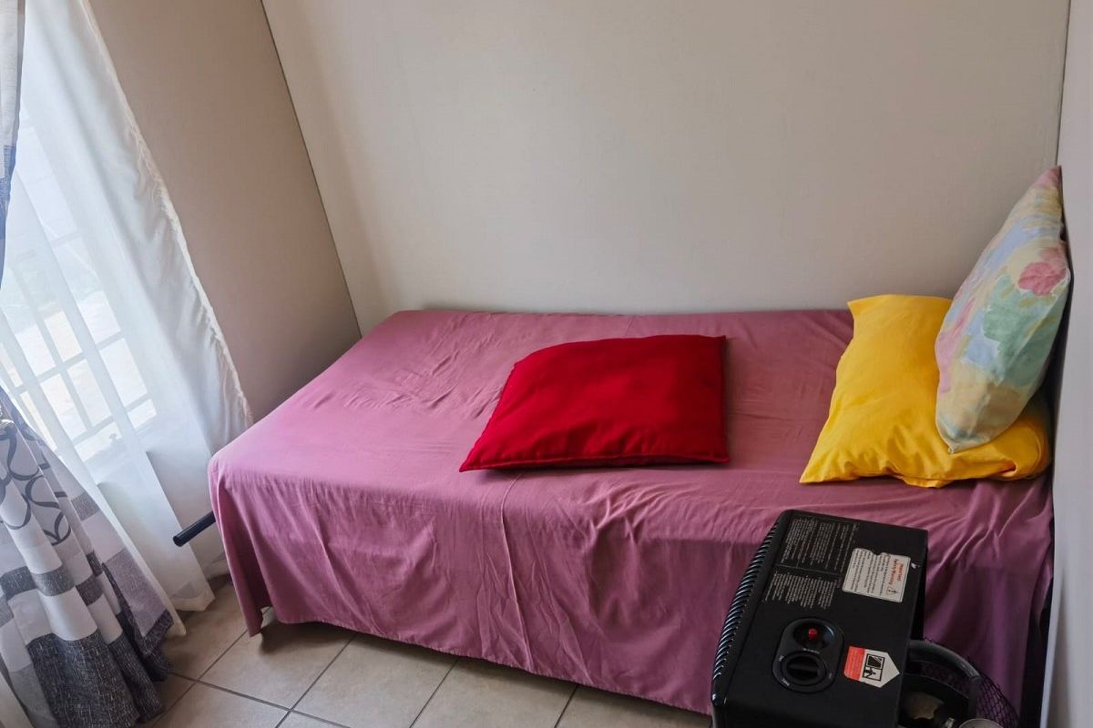 A compact bedroom featuring tiled flooring and a window with curtains, providing a functional space for a single bed.