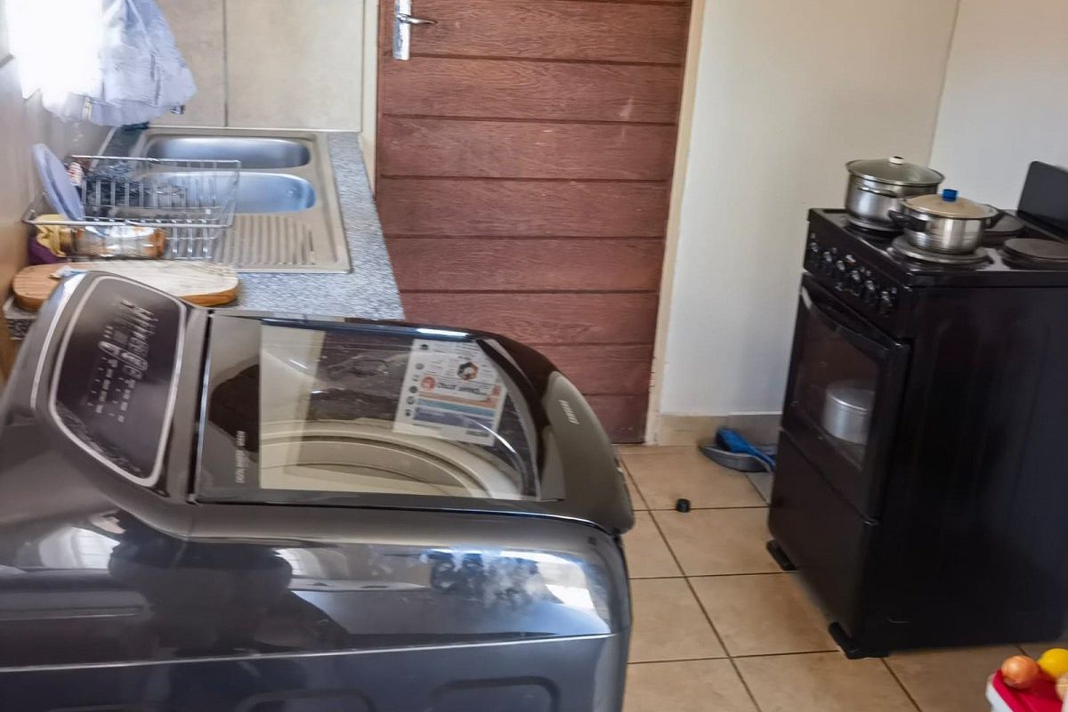 A functional kitchen area featuring a double stainless steel sink, tiled flooring, and space for a freestanding stove and laundry appliance.