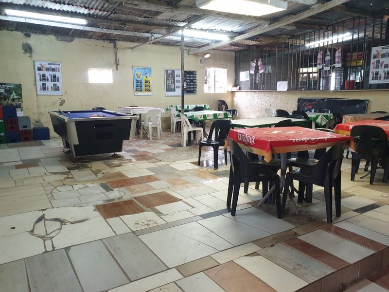 A spacious clubhouse or entertainment area featuring tiled flooring, exposed corrugated metal ceiling, and industrial-style lighting, currently set up with tables and a pool table.