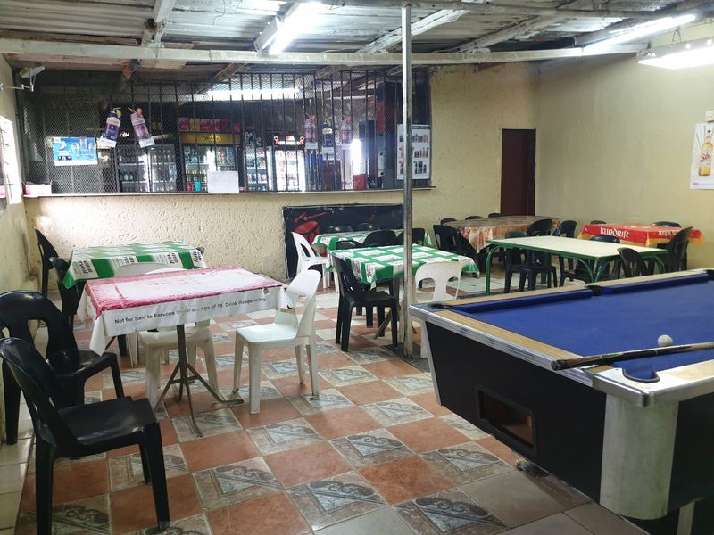 A functional bar area featuring tiled flooring, security grilles, and exposed ceiling structure, currently set up with multiple tables and a pool table.
