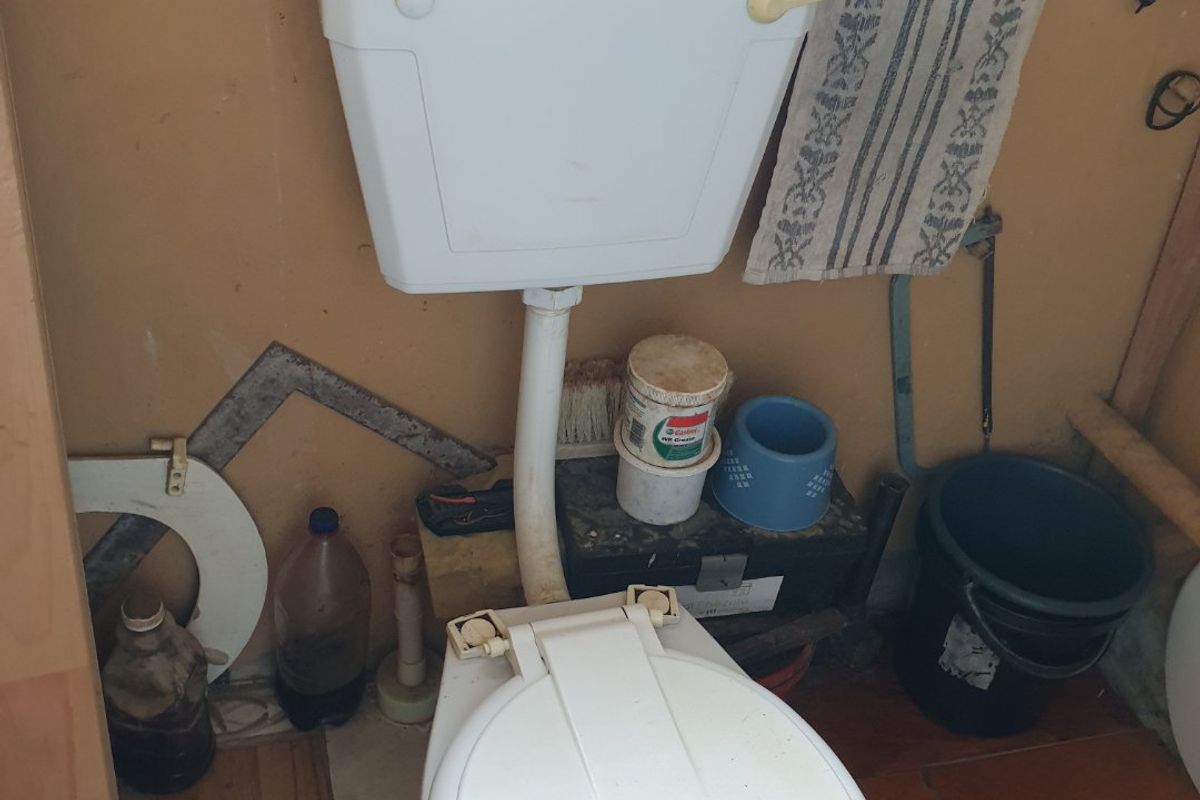 A small bathroom featuring a standard ceramic toilet with a cracked seat and tiled flooring, currently in need of maintenance and cosmetic updates.