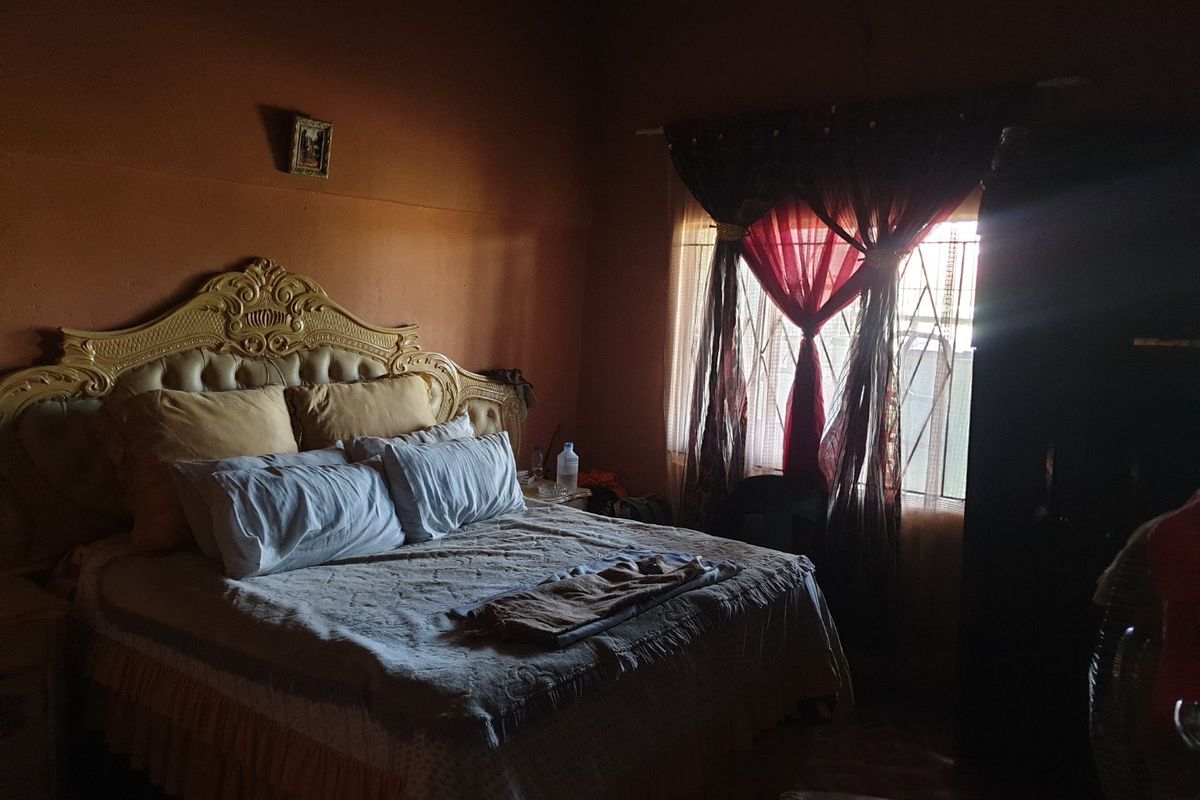 A dimly lit bedroom featuring a window with security bars and dark curtains.