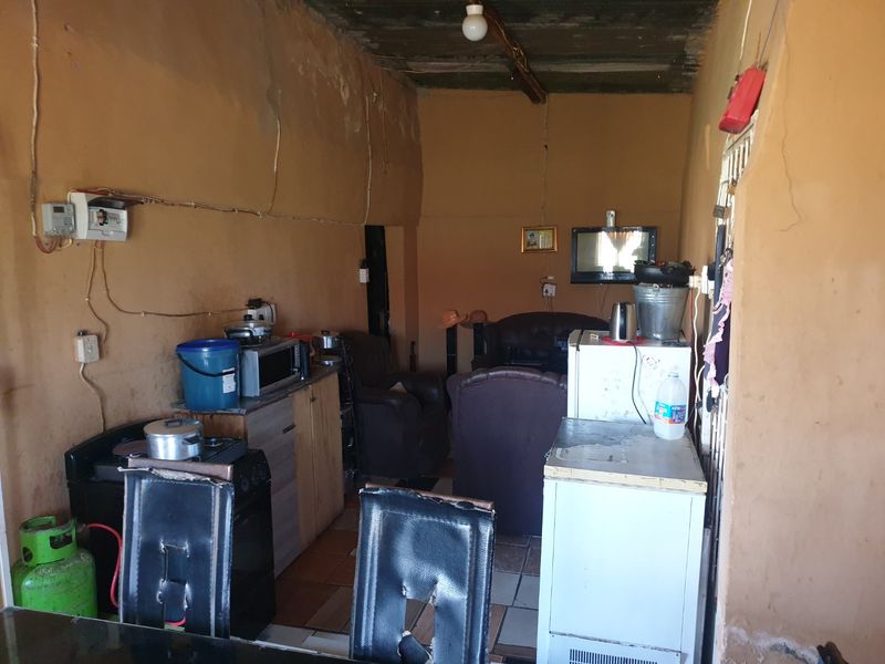 Open plan living and kitchen area featuring tiled flooring and exposed concrete ceiling, requiring significant cosmetic renovation and wall repairs.