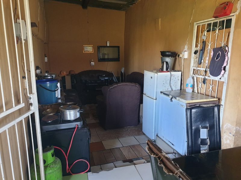 An open-plan living and kitchen area featuring tiled flooring and a security gate, currently in need of maintenance and cosmetic updates.