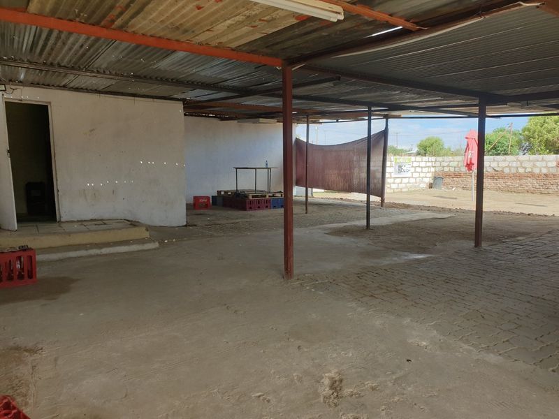A large, covered outdoor patio area featuring a corrugated metal roof, steel support columns, and concrete flooring, suitable for renovation or outdoor entertainment.