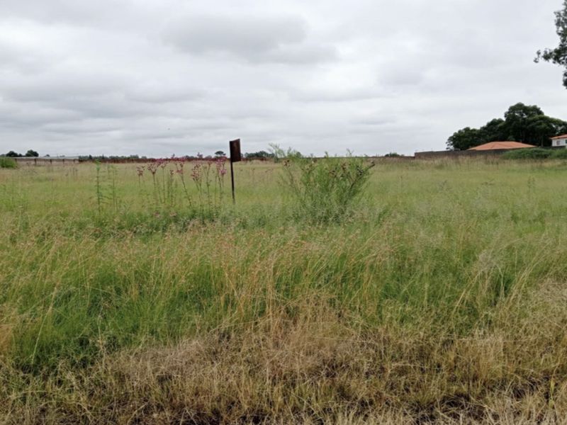 A vacant residential plot of land featuring open grass and a perimeter wall, offering a blank canvas for future development.