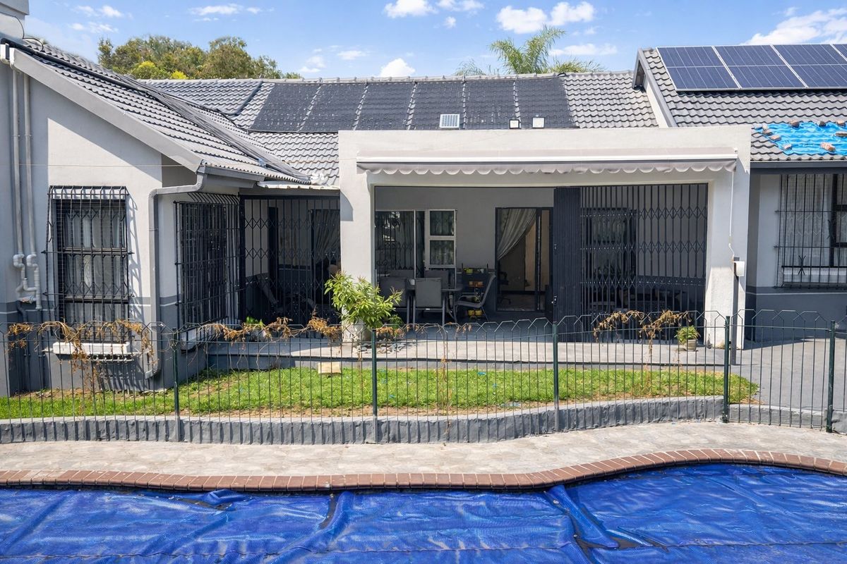 Rear view of the property featuring a swimming pool with cover, a covered patio area, and solar panels installed on the tiled roof.