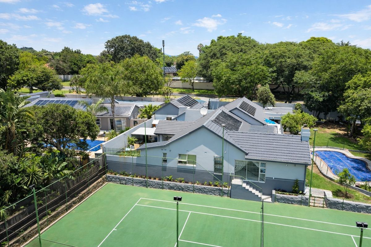 Aerial view of a residential property featuring a private tennis court, swimming pool, solar panel installation, and well-maintained garden areas.
