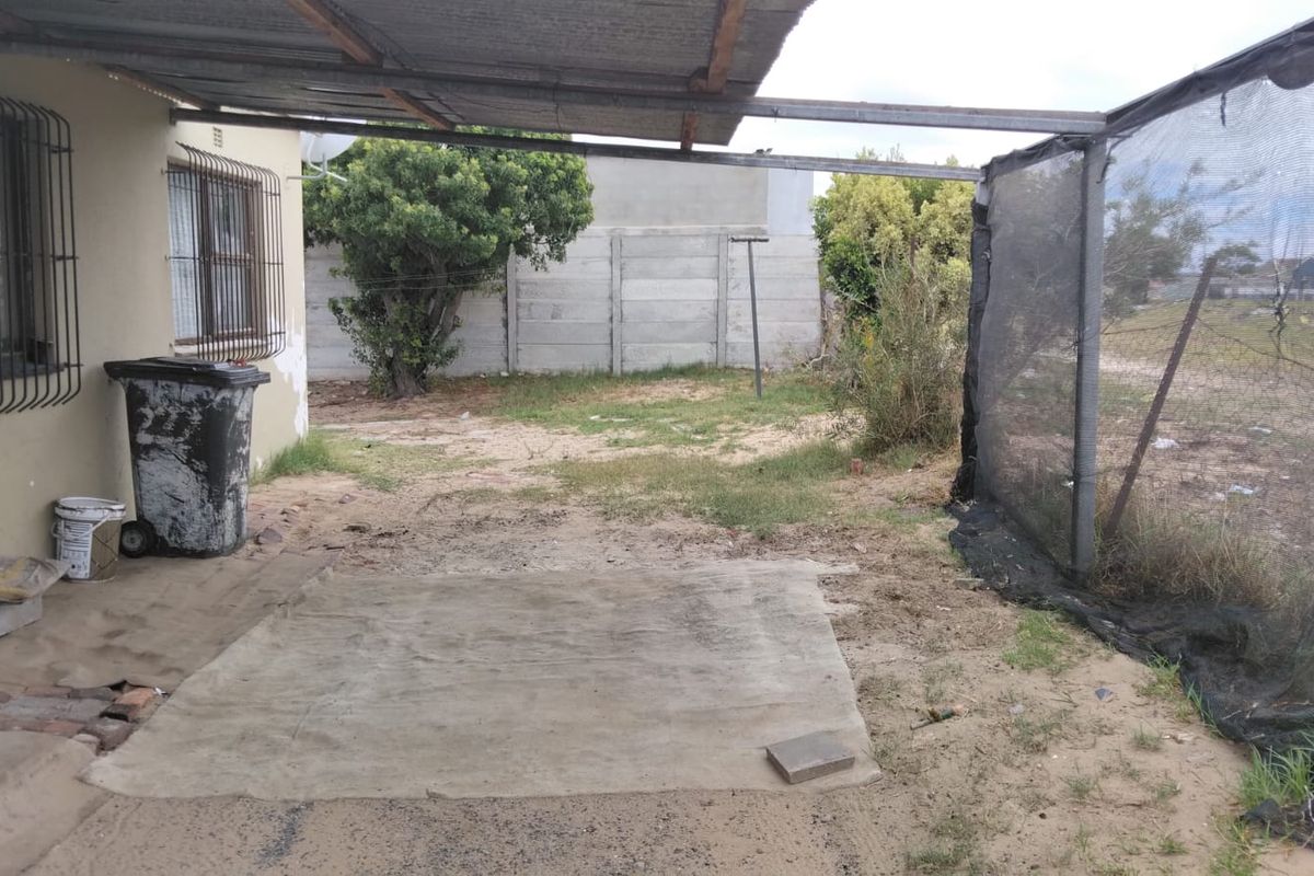 A covered outdoor patio area featuring a metal roof structure, security bars on windows, and a partially enclosed yard with concrete boundary walling.