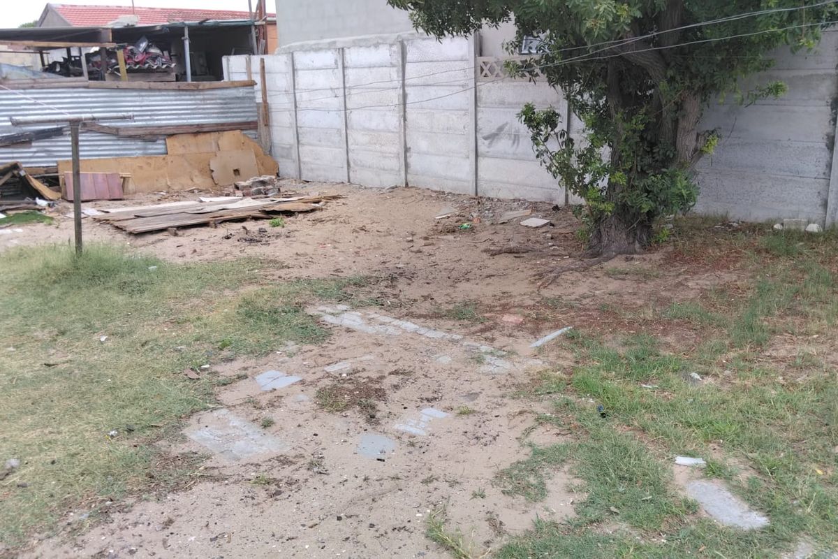 A rear garden area featuring a precast concrete boundary wall, a mature tree, and significant space requiring landscaping and debris removal.