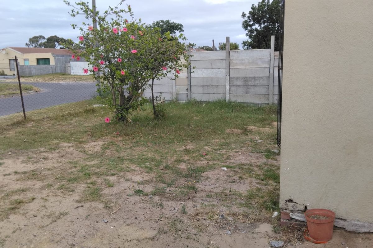 A view of the rear yard featuring a precast concrete boundary wall, wire fencing, and an exterior wall showing signs of plaster damage.