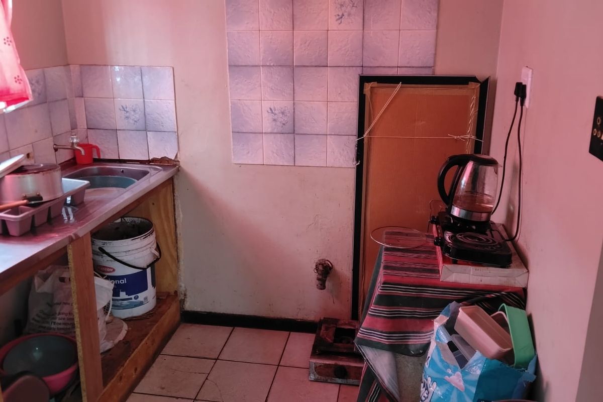A compact kitchen area featuring a stainless steel sink, tiled splashback, and ceramic floor tiles, currently requiring significant maintenance and cosmetic updates.