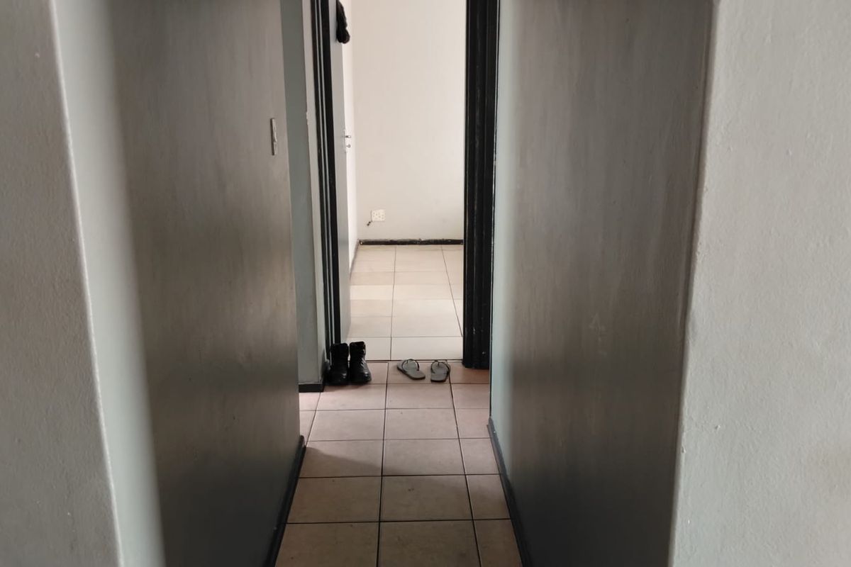 A narrow interior hallway featuring neutral wall paint and ceramic floor tiling, providing access to adjacent rooms.