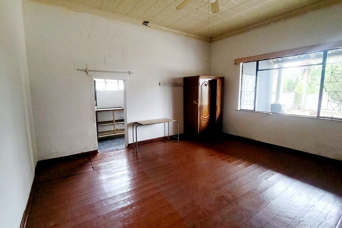 A spacious bedroom featuring original timber flooring, a ceiling fan, and a large window, offering a blank canvas for renovation and modernization.