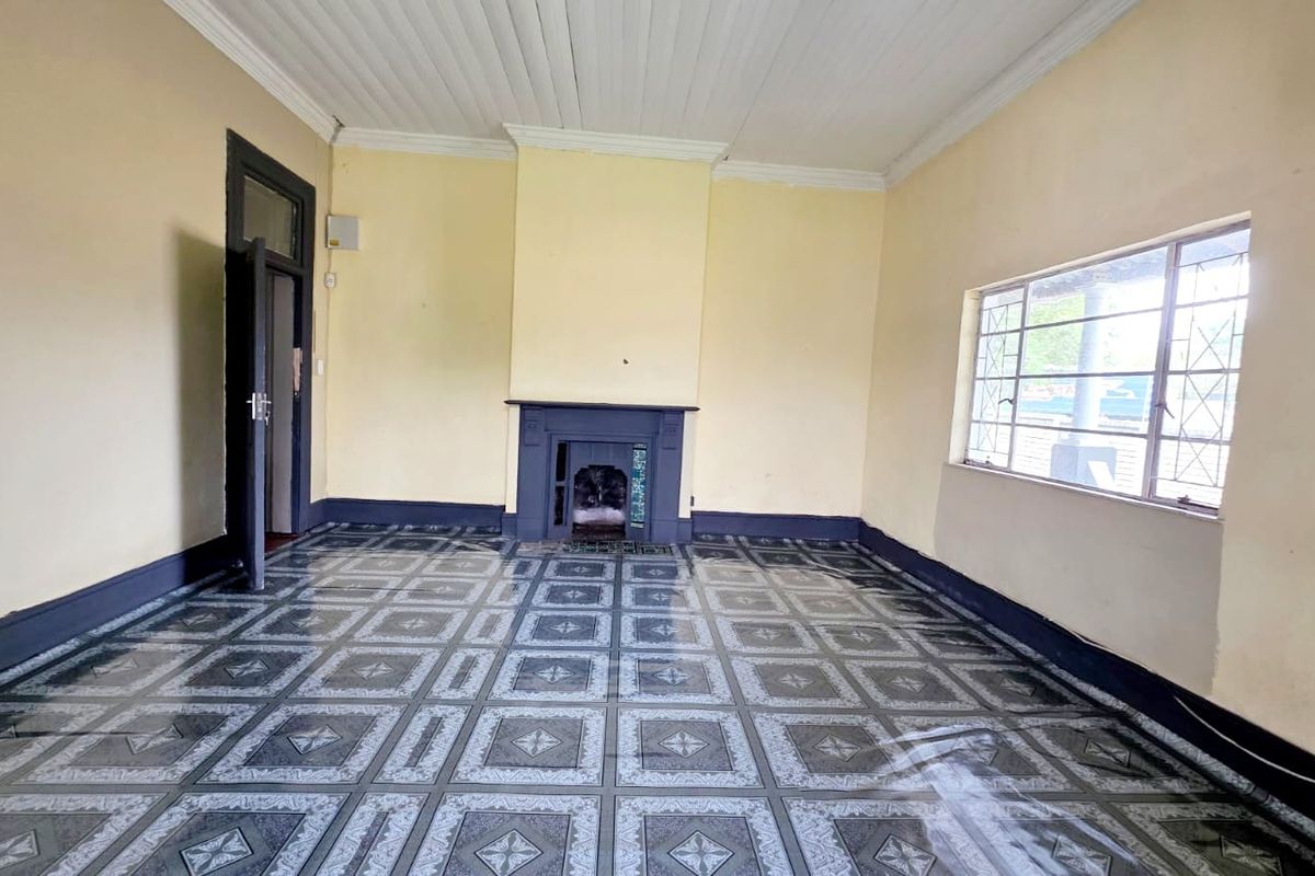 An empty living room featuring a central fireplace, patterned tiled flooring, and a timber-paneled ceiling with traditional cornice detailing.