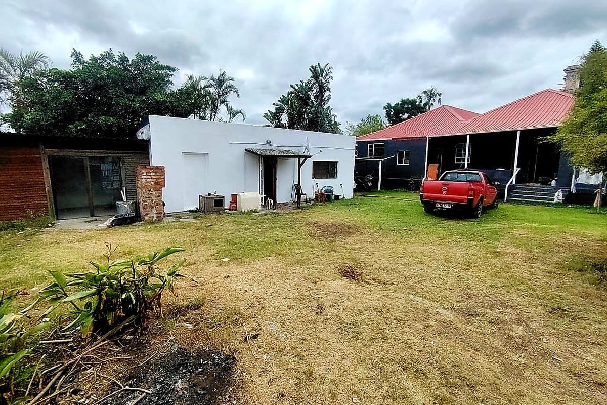 Rear view of the property showing a large garden area, a detached outbuilding, and the main house with a covered veranda.
