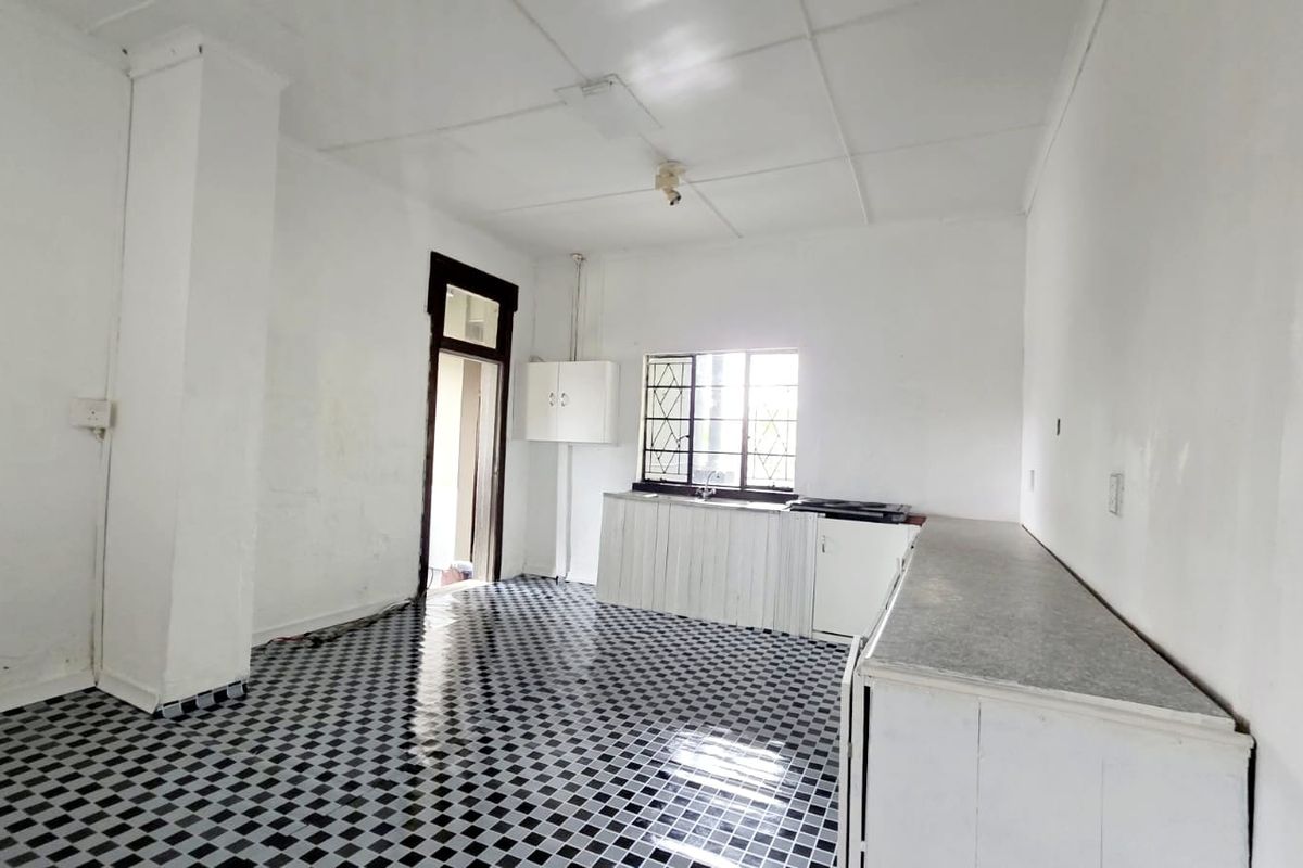 An empty, dated kitchen featuring basic cabinetry, laminate countertops, and a checkerboard tiled floor, offering a blank canvas for renovation.