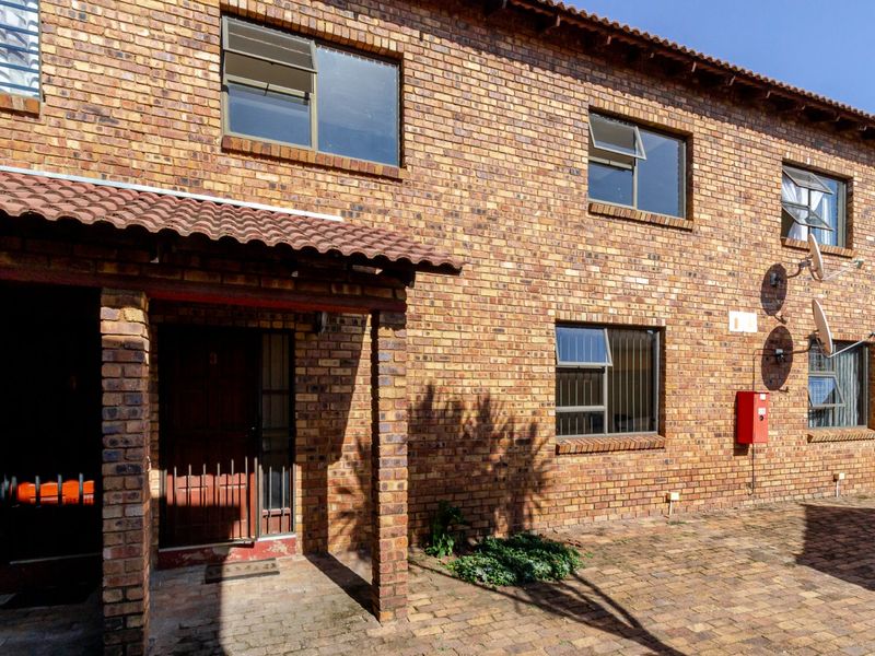 Front elevation of a face brick townhouse featuring a covered entrance, paved driveway, and aluminium window frames.