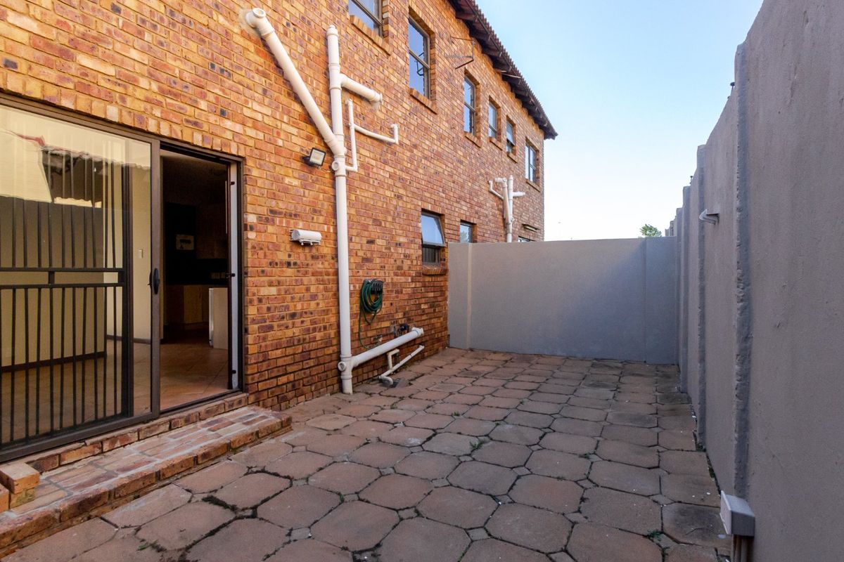 A rear exterior view of the townhouse featuring a paved patio area, exposed brick facade, and sliding door access to the interior.
