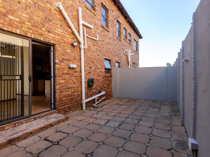 A rear exterior view of the townhouse featuring a paved patio area, exposed brick facade, and sliding door access to the interior.
