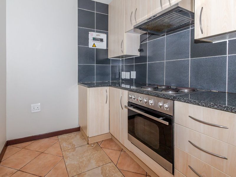 Compact kitchen featuring light wood cabinetry, granite countertops, a built-in oven with electric hob, and dark tiled backsplash.