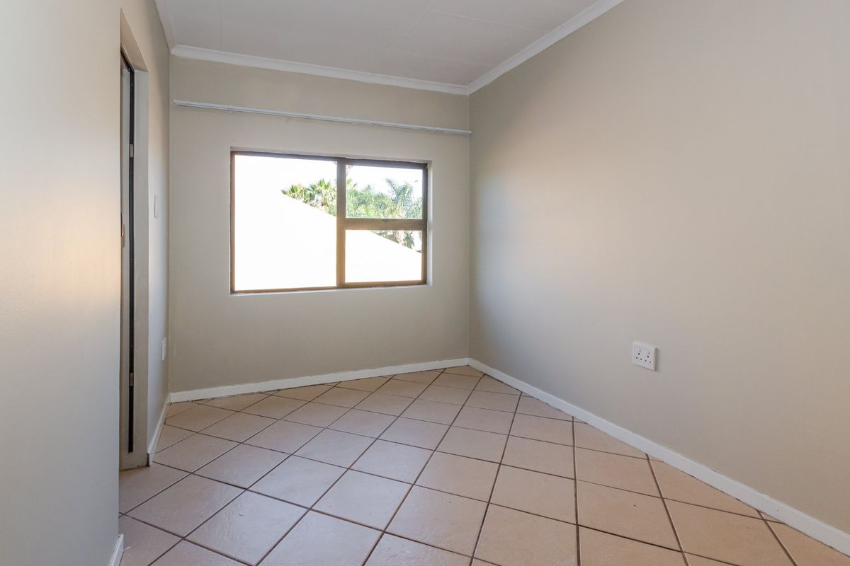 A clean, empty bedroom featuring neutral wall paint, tiled flooring, and a window with a curtain rail.