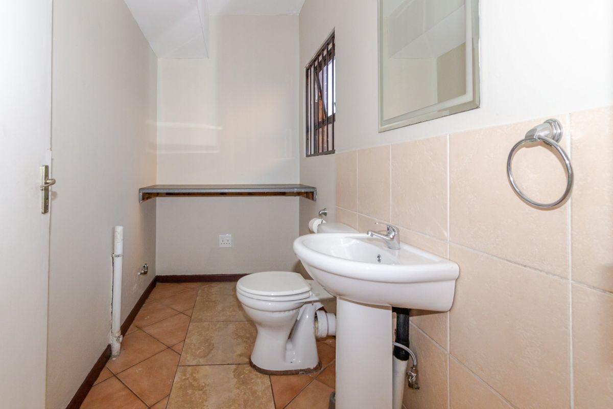 A compact guest bathroom featuring a pedestal basin, toilet, tiled finishes, and a wall-mounted mirror, requiring minor cosmetic updates to improve its overall presentation.