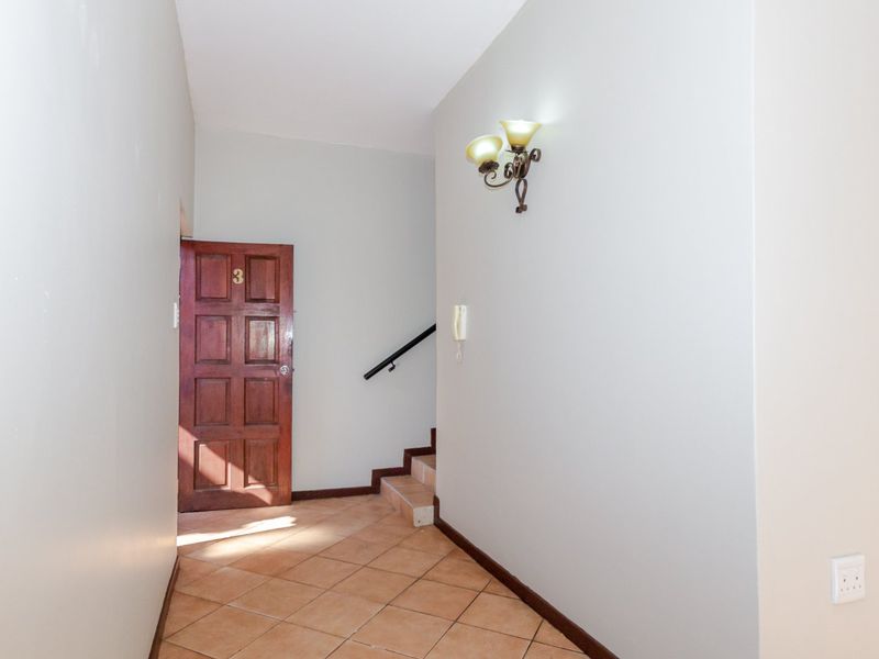 A clean and functional entrance foyer featuring tiled flooring, a timber front door, and a staircase leading to the upper level.