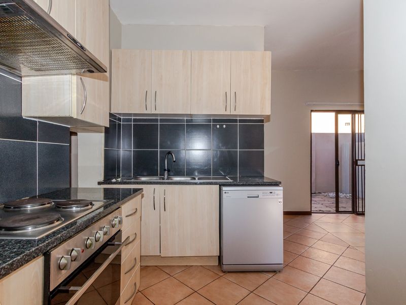 A functional kitchen featuring light wood cabinetry, granite countertops, a tiled backsplash, and direct access to an outdoor patio area.