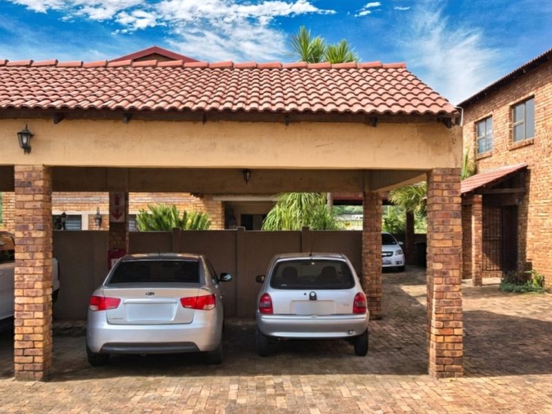A covered carport area featuring brick pillars and a tiled roof, providing sheltered parking space within the townhouse complex.